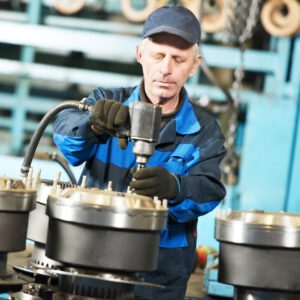 Montagemitarbeiter in blauer Arbeitskleidung verschraubt präzise Maschinenteile in einer industriellen Fertigungshalle.