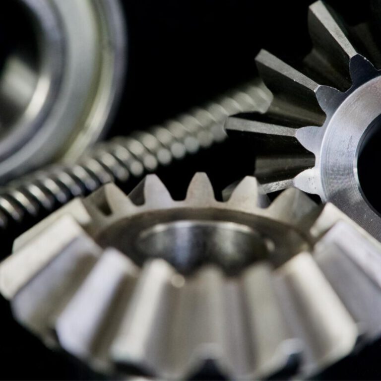 Makroaufnahme mehrerer Präzisionszahnräder und Gewindespindeln aus Metall. Die scharfen Zähne und glänzenden Oberflächen zeigen die hohe Fertigungsqualität typischer Komponenten der Antriebs- und Lineartechnik.